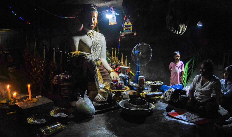 Une statue de Lok Yeay Mao éclairée à la bougie dans les grottes près de Kampong Trach, avec une diseuse de bonne aventure et une famille assises à proximité