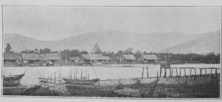 View across the river at Kampot in the 1880s, with boats in the foreground and low buildings backed by hills